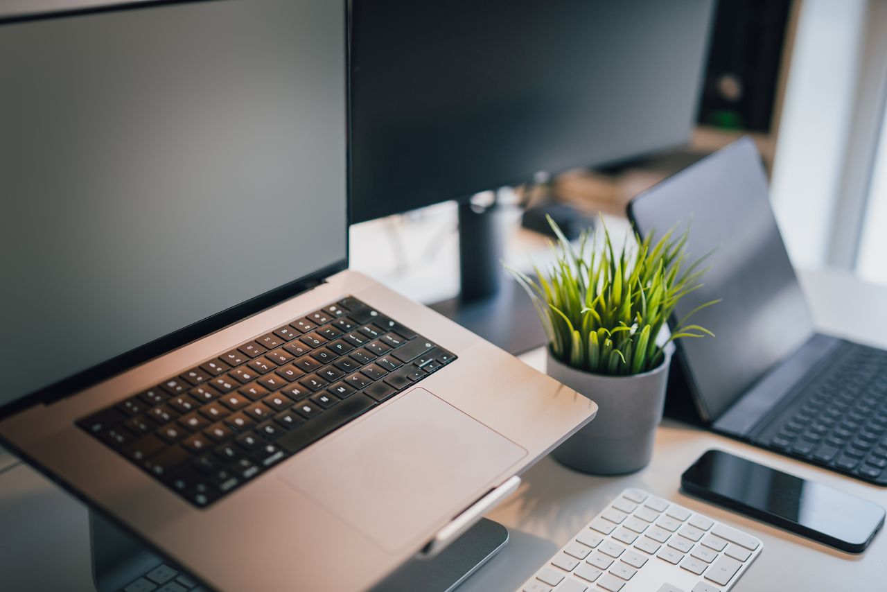 The Art of Drawing Readers In: Your attractive post title goes here A sleek office workspace featuring a laptop, smartphone, keyboard, and potted plant for productivity.